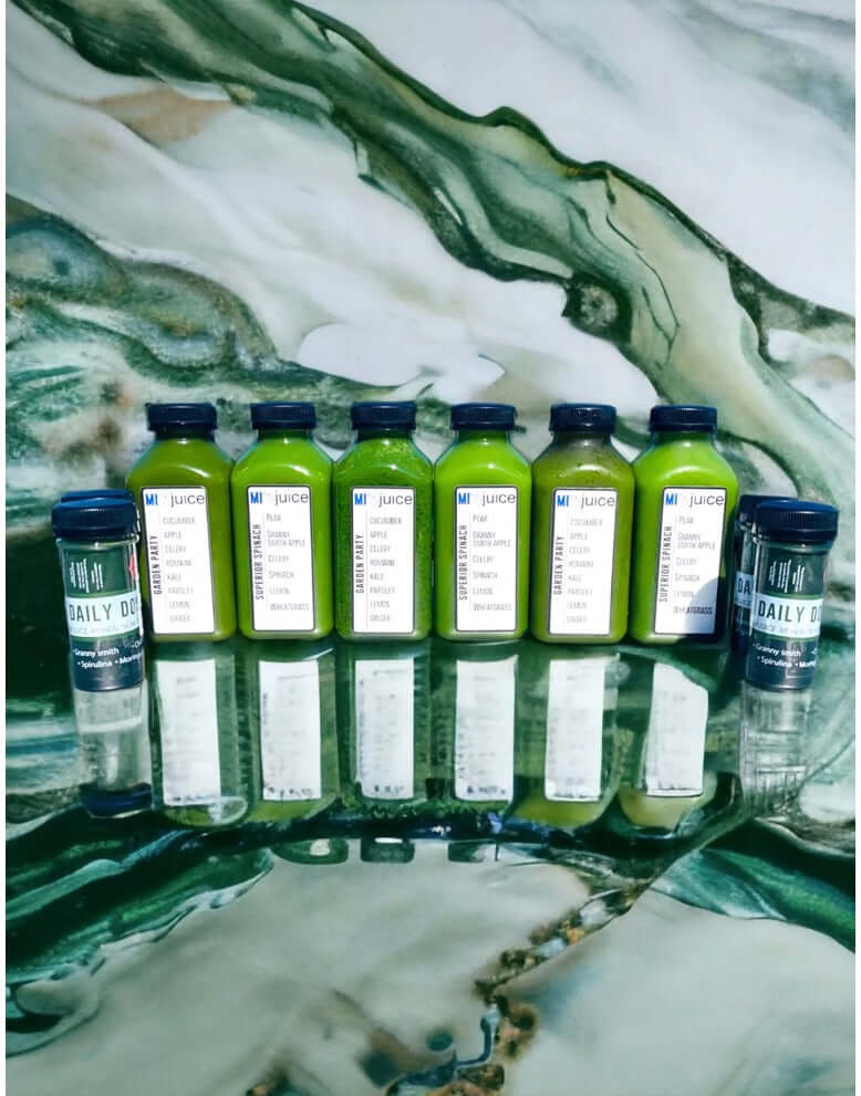 Array of organic cold-pressed juices and Daily Dose on a reflective surface, made with local produce.